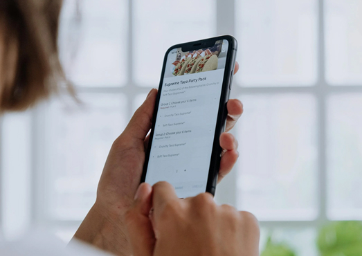 Persona usando un smartphone para navegar un menú digital de restaurante, mostrando opciones de selección de platos.