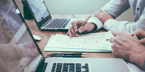 Personas trabajando en equipo, revisando documentos y datos en una computadora portátil, simbolizando colaboración y análisis en proyectos tecnológicos.