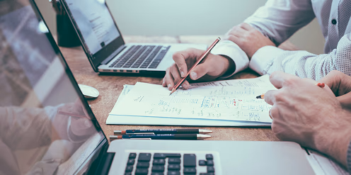 Personas trabajando en equipo, revisando documentos y datos en una computadora portátil, simbolizando colaboración y análisis en proyectos tecnológicos.